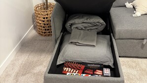 Ein graues Sofa mit Stauraum darunter, ein gewebter Korb und eine grüne Pflanze.