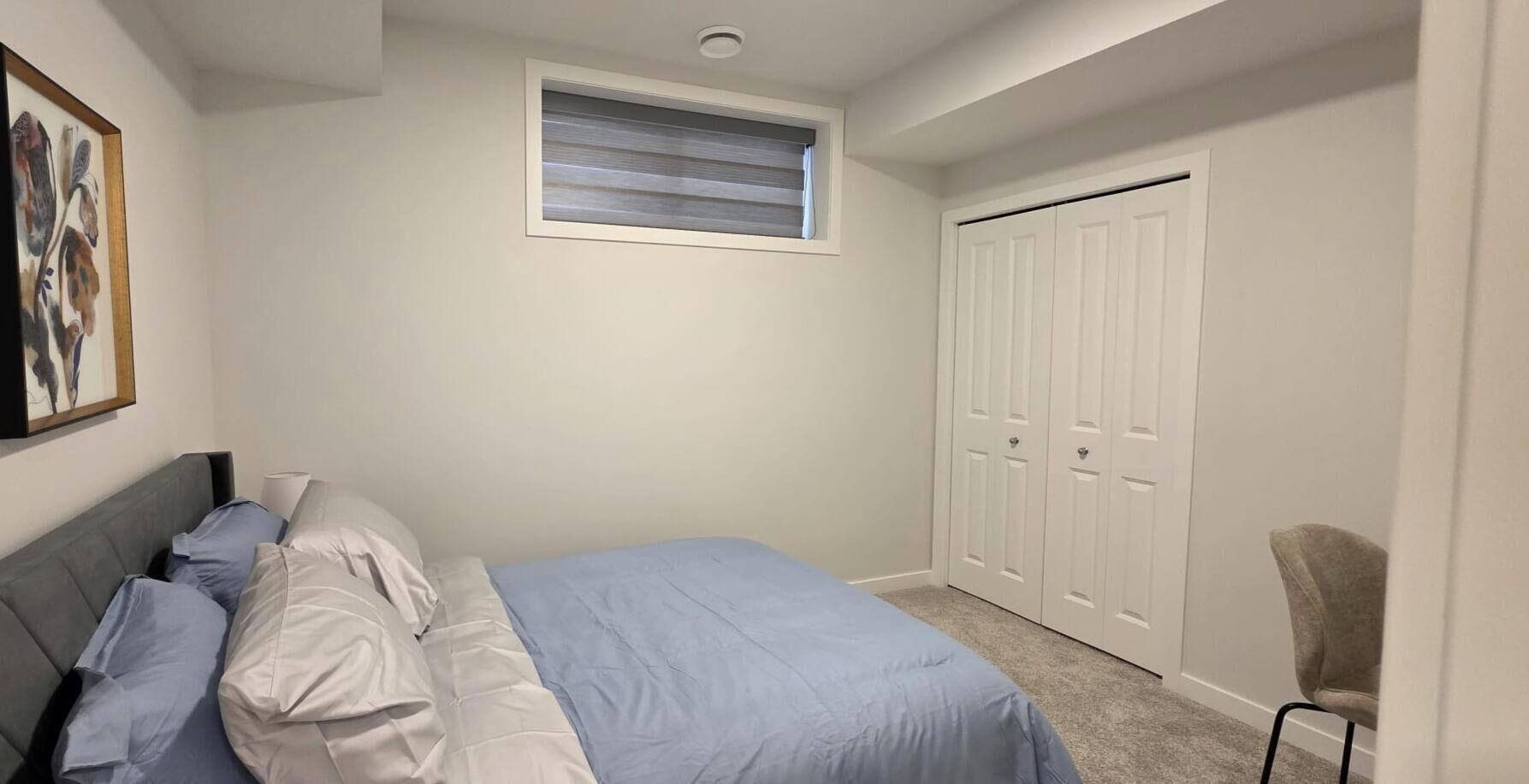 A bedroom with a bed, a chair, a wardrobe, and a window.