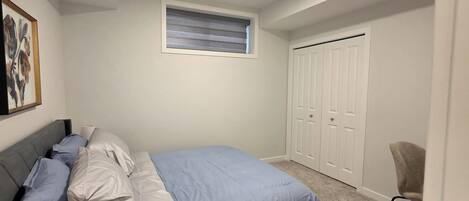 A bedroom with a bed, a chair, a wardrobe, and a window.