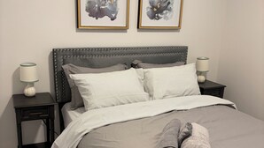 Ein ordentlich bezogenes Bett mit Streifenmuster, zwei Nachttische mit Lampen und zwei gerahmte abstrakte Gemälde an der Wand.