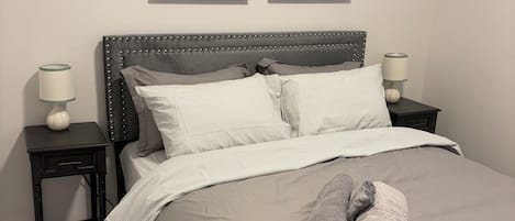 A neatly made bed with striped bedding, two bedside lamps, and two framed abstract paintings on the wall.