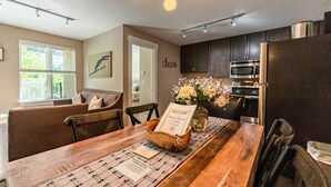 Una cocina moderna con armarios oscuros, un refrigerador de acero inoxidable y un comedor con una mesa y sillas de madera.
