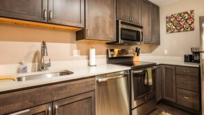 Una cocina con armarios de madera oscura, electrodomésticos de acero inoxidable, un microondas y una cafetera.