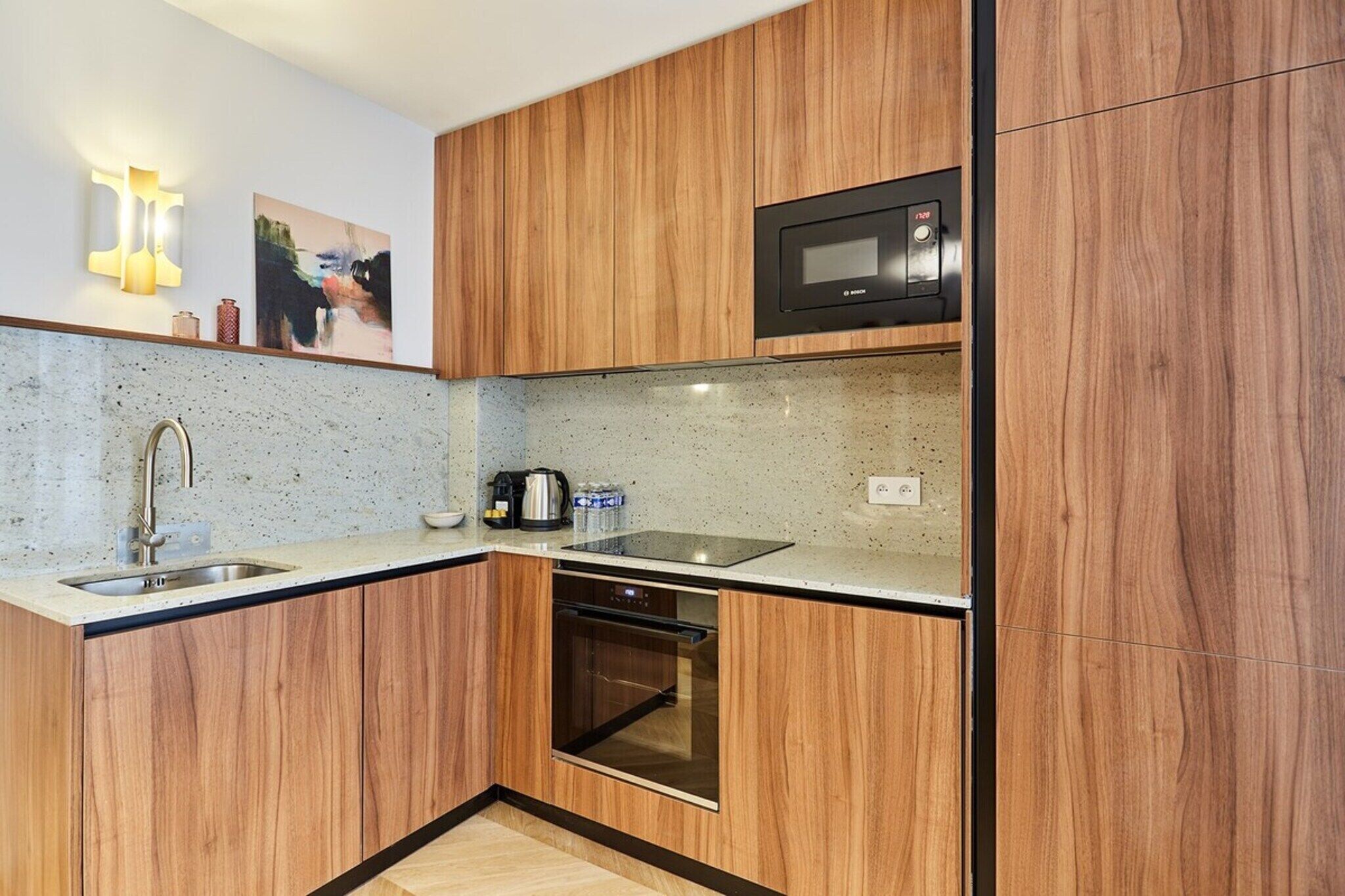 A compact kitchen with wooden cabinets, a microwave, a sink, and a built-in oven.