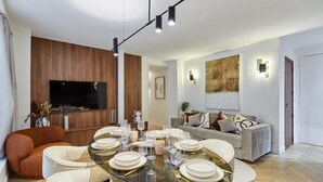 Un soggiorno moderno con un tavolo da pranzo in vetro apparecchiato per sei persone, un divano, una televisione e una parete d'accento in legno.