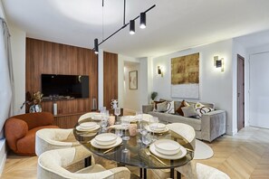 A modern living room with a glass dining table set for six, a sofa, a television, and a wooden accent wall. - Stunning apartment  with AC - Center of Paris (Paris)