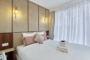 A hotel room with a bed, two wall-mounted light fixtures, a bedside table, and a window with sheer curtains. - Stunning apartment  with AC - Center of Paris (Paris)