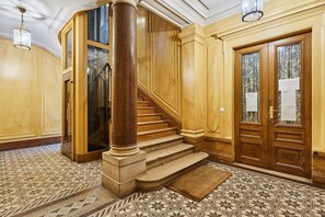 A grand staircase with marble steps and a wooden handrail, leading to a room with a patterned floor and a large wooden door with a glass panel. - Stunning apartment  with AC - Center of Paris (Paris)