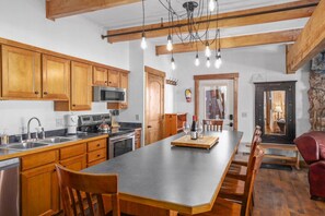 A kitchen with wooden cabinets, a central island, stainless steel appliances, and a dining area with chairs. - The Whetstone Chalet; Mtn Views, Walk to Slopes (Crested Butte)