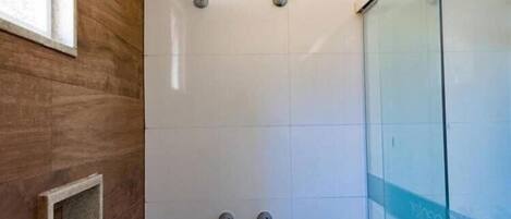 Una ducha con cerramiento de vidrio, pared de panel de madera y un estante pequeño.