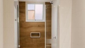 Une salle de bain avec une douche, un mur en bois, une fenêtre et un sol carrelé.