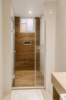Un baño con ducha, pared de madera, ventana y piso de baldosas.