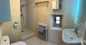 Une salle de bain comprenant des toilettes, une douche, un porte-serviettes, une petite fenêtre et un lavabo.