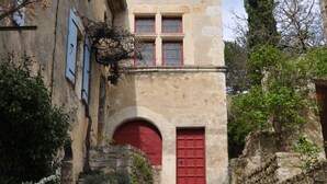 Un bâtiment en pierre avec une porte et des fenêtres rouges, un chemin pavé et une végétation luxuriante tout autour.