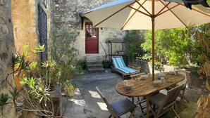 Une terrasse avec une table, des chaises, un parasol, un fauteuil de relaxation et des plantes en pot.