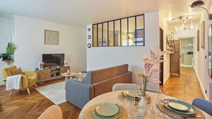 Un salon moderne avec un canapé, un téléviseur et un coin repas, où une table est dressée pour deux personnes.