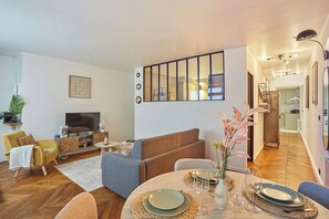 A modern living room with a sofa, television, and dining area with a table set for two. - Superb apartment Center of Paris (Paris)