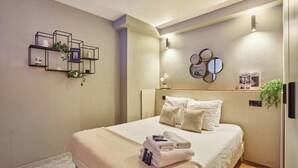Une chambre à coucher bien rangée, avec un lit, des oreillers, une table de chevet, une étagère murale ornée d’objets décoratifs et un miroir.