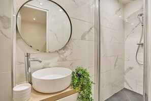 A bathroom with a round mirror, a white sink, a shower, and a small green plant. - Superb apartment Center of Paris (Paris)
