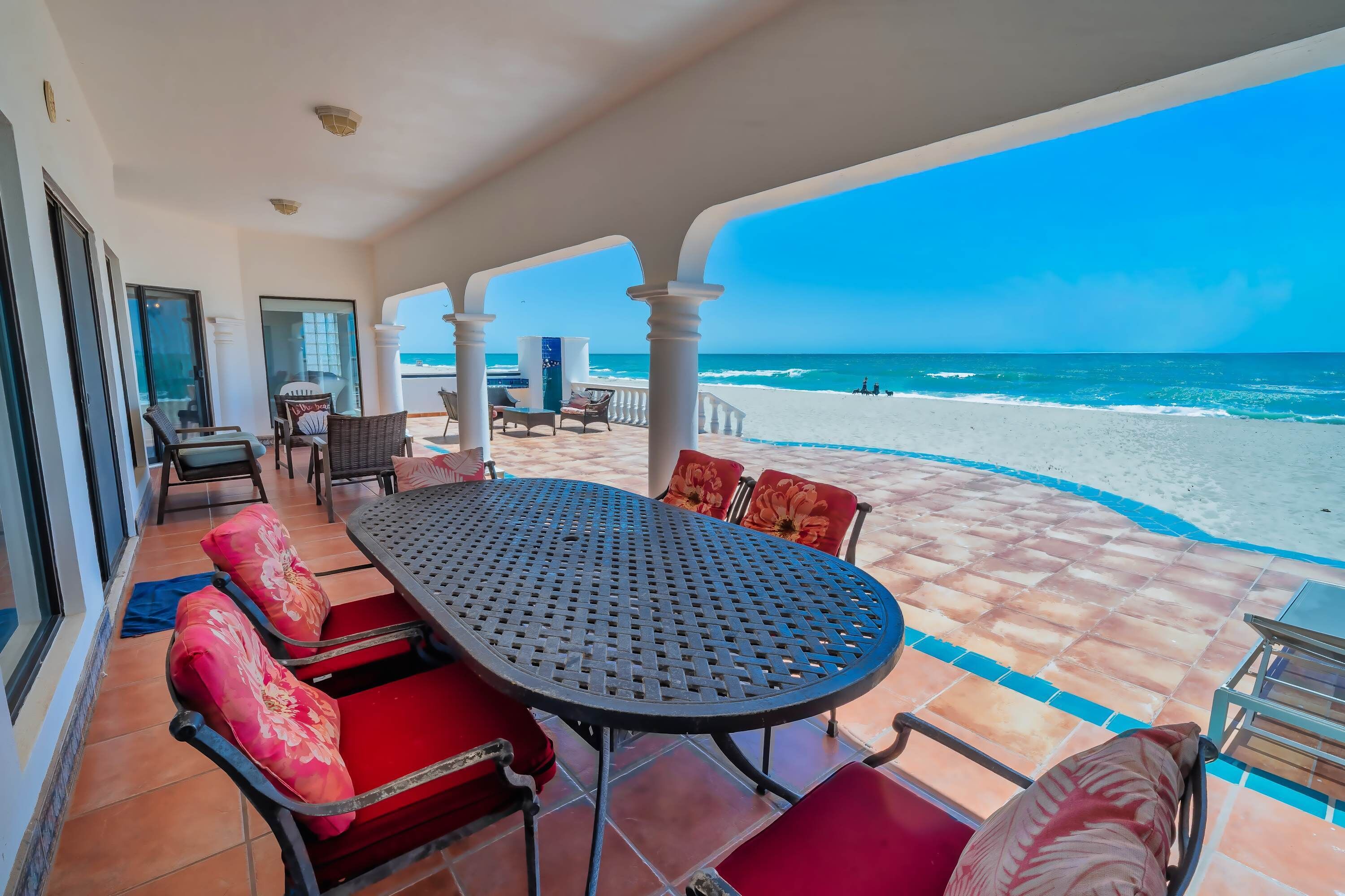 Un espace extérieur abrité, avec une table et des chaises, donnant sur une plage.