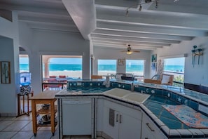 A kitchen with a view of the beach, a dining area with a table and chairs, and a ceiling fan. - Casa La Paz|Beachfront in Playa La Jolla|10 Guests (Playa Encanto)