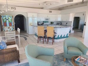 Amplia sala de estar con isla de cocina, sillas de mimbre y una mesa de comedor.