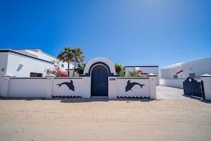 A building with a white facade, a central entrance with a black door, and two dolphin silhouettes on the walls. - Casa La Paz|Beachfront in Playa La Jolla|10 Guests (Playa Encanto)