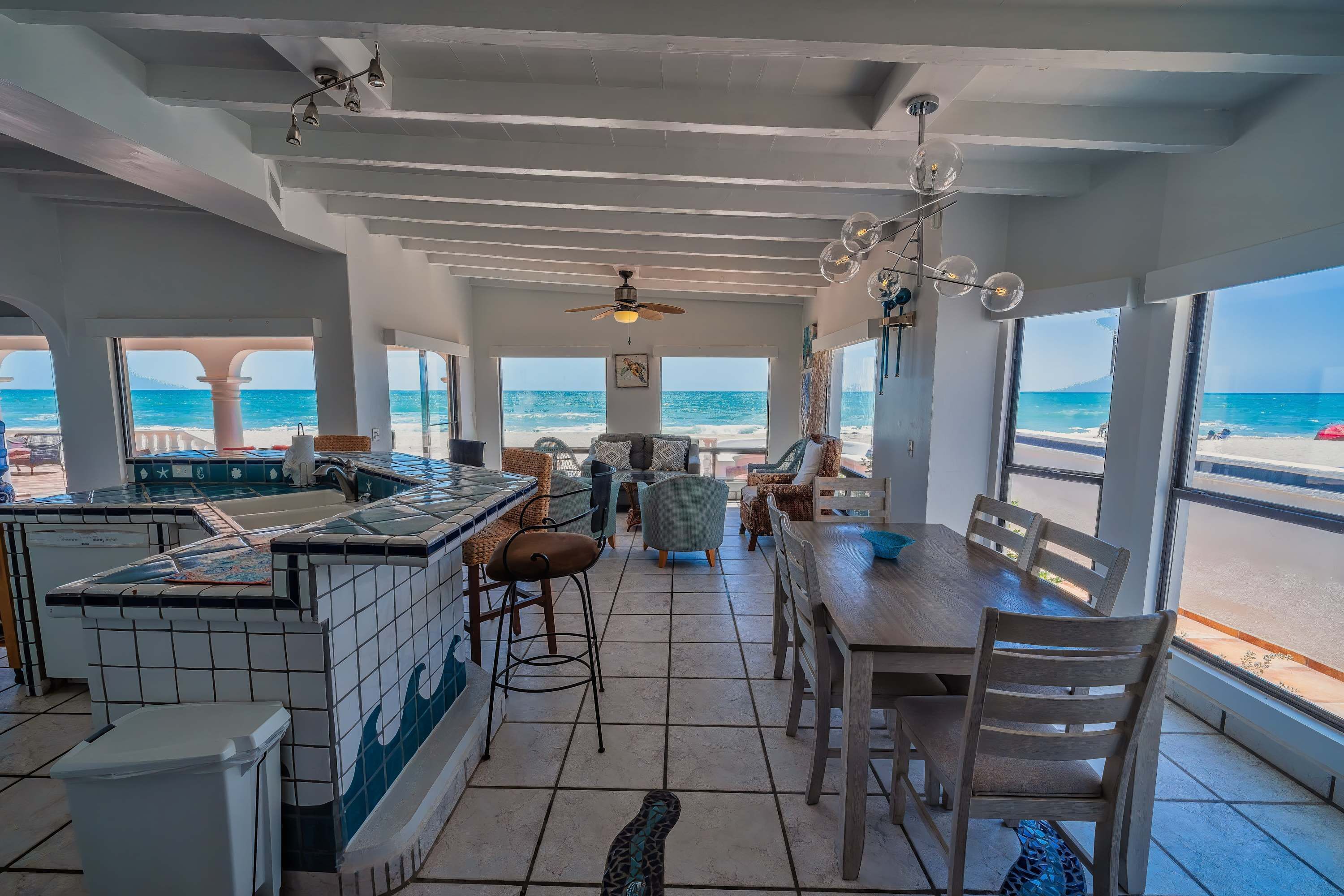 Un bar situé en bord de mer, offrant une vue sur l’océan, doté d’un ventilateur de plafond et d’un espace repas avec des chaises et une table.