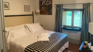 Een slaapkamer met een bed, een raam met gordijnen, een wandlamp en ingelijste foto's.