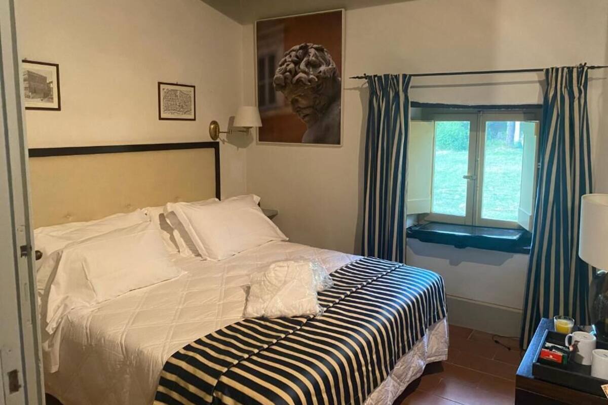 A bedroom with a bed, a window with curtains, a wall-mounted lamp, and framed pictures.