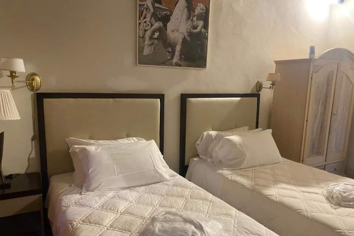 Two beds with headboards, a lamp, a painting, and a wardrobe.
