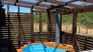 Eine Holzterrasse mit Whirlpool, Tisch und einer Pergola.