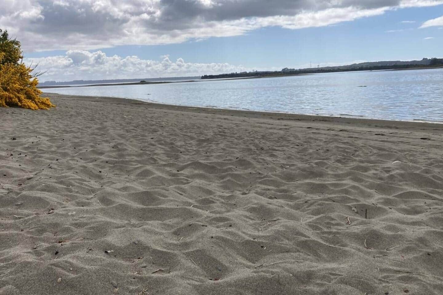 A sandy beach with a calm body of water and a distant shoreline.