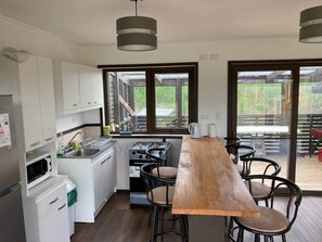 A modern kitchen with white cabinets, a wooden dining table, and a view of the outdoors.