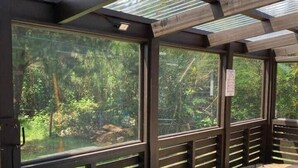 A covered outdoor seating area with tables and benches, large windows, and a view of a forested area. - Fully equipped cabin in Chiloé, steps from the beach (Ancud)