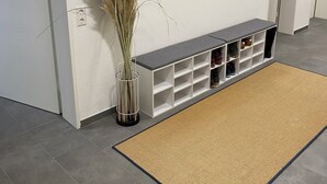 Un corridoio con parete bianca, uno specchio, un portavasetti per scarpe e un vaso con piante essiccate.