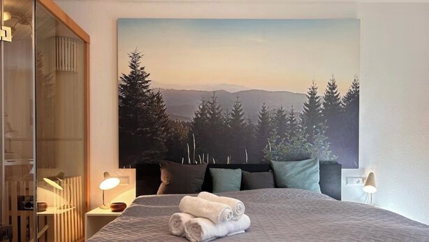 Una camera da letto con un grande letto, un quadro raffigurante una foresta e un'armadio in legno.