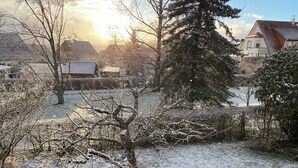 Un quartiere residenziale con terreno innevato, alberi spogli e case con tetti in tegole rosse.