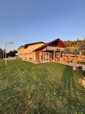 Ein zweistöckiges GebĂ€ude mit Balkon, ĂŒberdachter Terrasse und RasenflĂ€che.