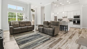 Ein geräumiges Wohnzimmer mit großem Sofa, Essbereich und Küche mit weißen Schränken und modernen Geräten.