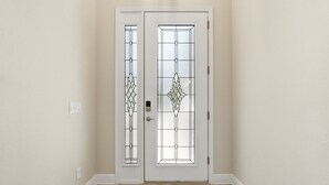 Eine weiße Tür mit einer Glasscheibe und Schlüsselloch, ein gemustertes Teppich auf dem Boden und ein Lichtschalter an der Wand.