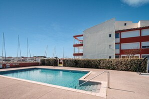 Una piscina amb un cel blau clar, un edifici amb façana vermella i blanca, i una tanca al fons.