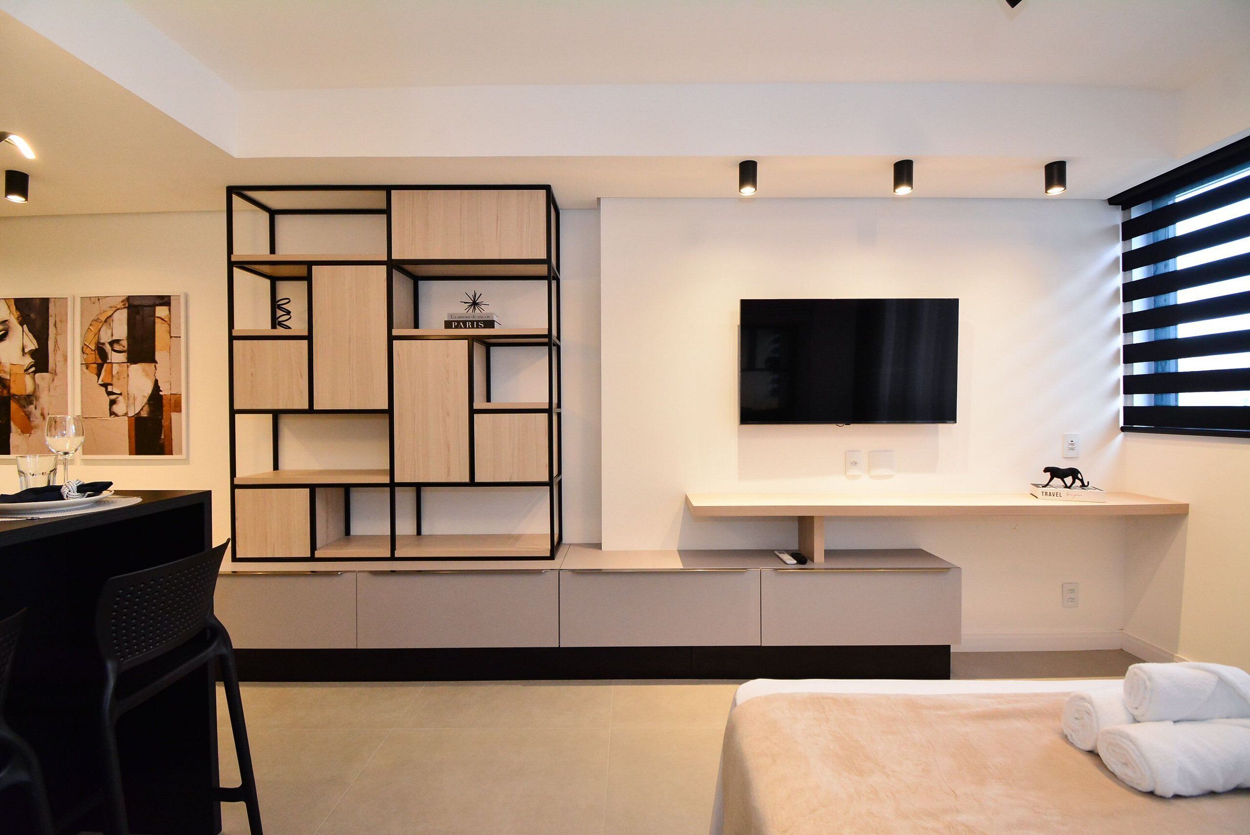 Una habitación de hotel moderna con una cama, un televisor montado en la pared, una estantería empotrada y un escritorio con una silla.