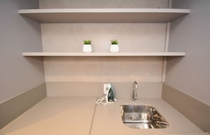 A modern kitchen with a stainless steel sink, a built-in ironing board, and two white vases on a shelf. - Studio em frente a UFSC e HU - VIVA 207R (Florianópolis)