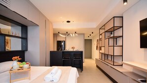 Una habitación de hotel moderna con cama, mesita de noche y una pequeña kitchenette.
