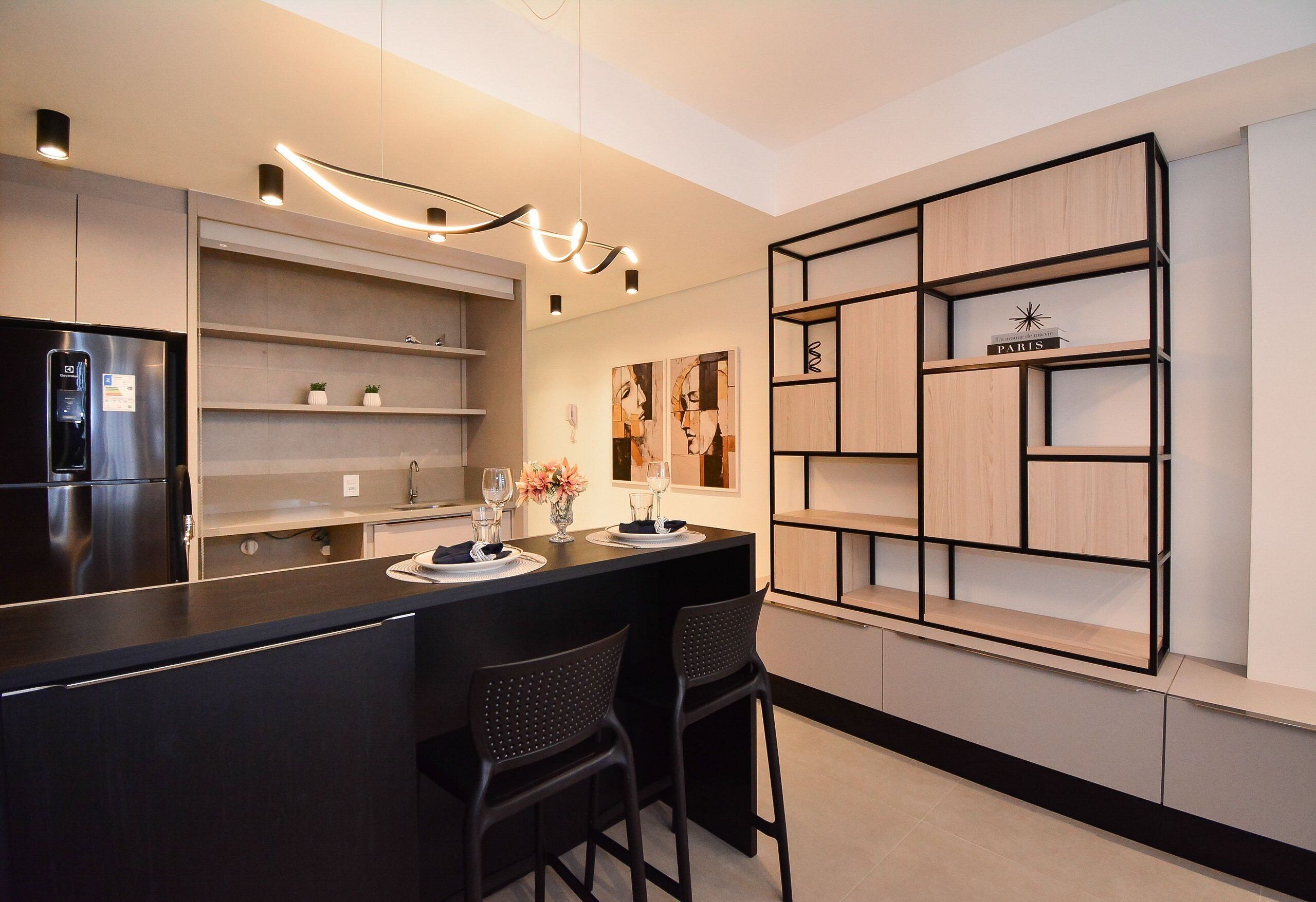 Una cocina moderna con una isla central, taburetes de bar, estanterías empotradas y un refrigerador.