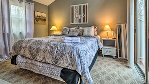 A bedroom with a large bed, two bedside lamps, a wall art piece, and a view of the outside through a window. - Walk to Locust Lake - Poconos Home w Fire Pit! (Pocono Lake)