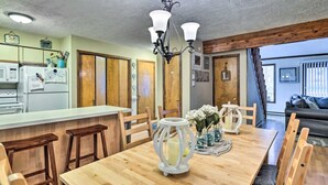 A dining area with a wooden table, white candle holders, and a kitchen in the background. - Walk to Locust Lake - Poconos Home w Fire Pit! (Pocono Lake)