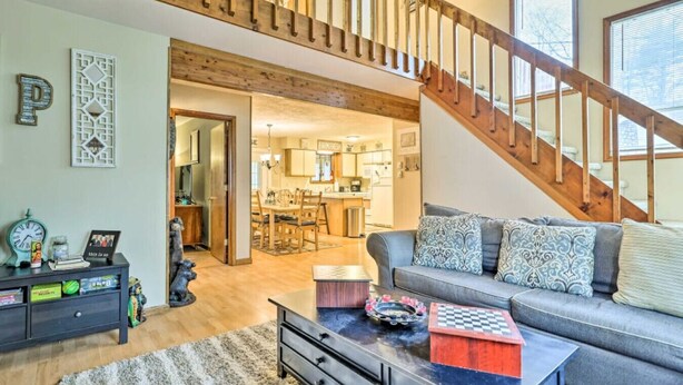A living room with a sofa, coffee table, and a staircase. - Walk to Locust Lake - Poconos Home w Fire Pit! (Pocono Lake)