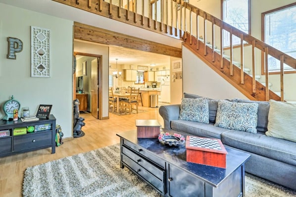 A living room with a sofa, coffee table, and a staircase. - Walk to Locust Lake - Poconos Home w Fire Pit! (Pocono Lake)